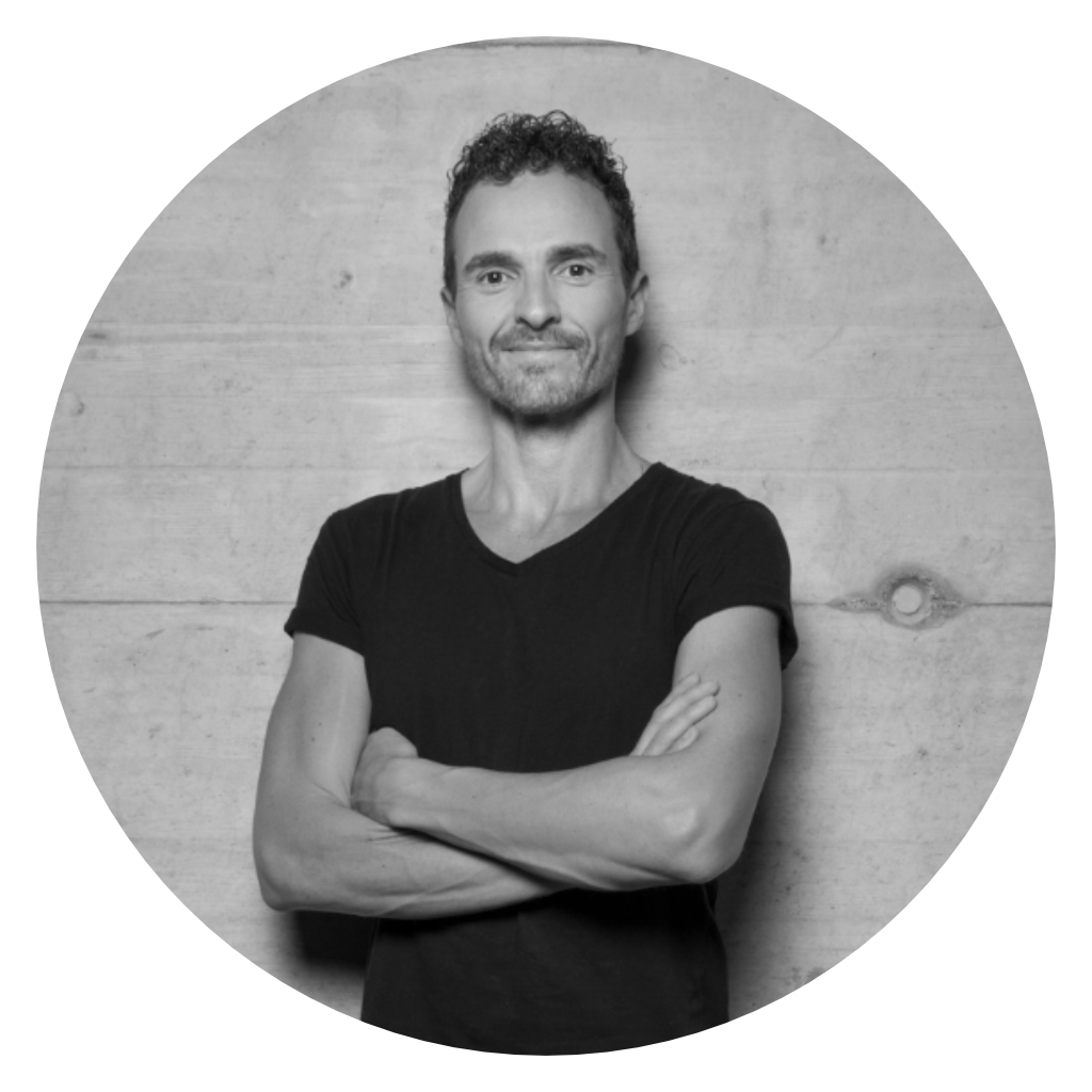Black-and-white portrait of a man with his arms crossed in front of a concrete wall, framed in a circular composition